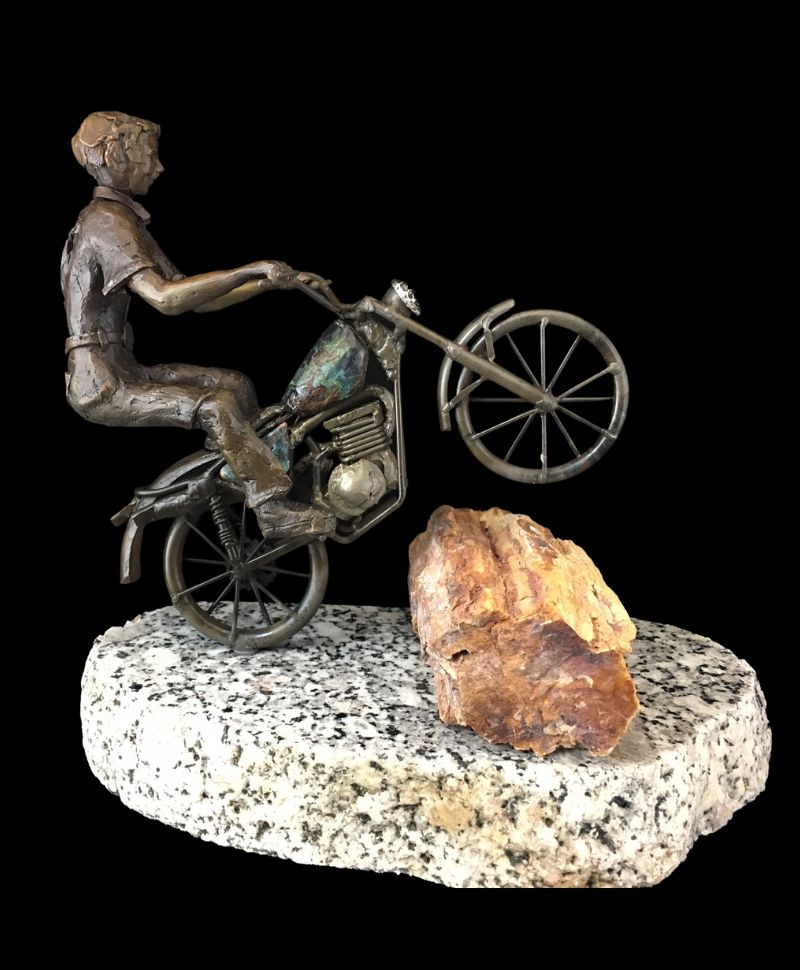 bronze sculpture of a boy riding a motorcycle over a log